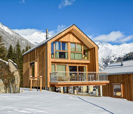 Chalets und Alpin Camping HOCHoben © ACM GmbH Modernes Holzhaus in verschneiter Berglandschaft unter blauem Himmel