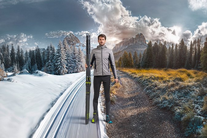 Langlauf Urlaub © Löffler GmbH Mann steht an der Grenze zwischen Schnee und Herbst mit Langlaufski