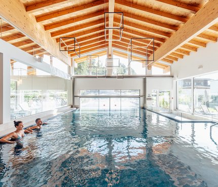 The Walchsee Resort Two people relaxing in indoor pool with wooden ceiling and large windows