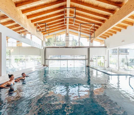 The Walchsee Resort Two people relaxing in indoor pool with wooden ceiling and large windows