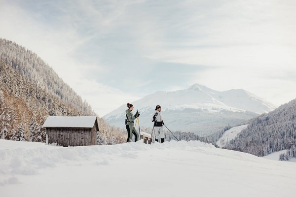 Italien © Alex Moling Zwei Personen beim Langlaufen im verschneiten Bergtal mit Hütten im Hintergrund