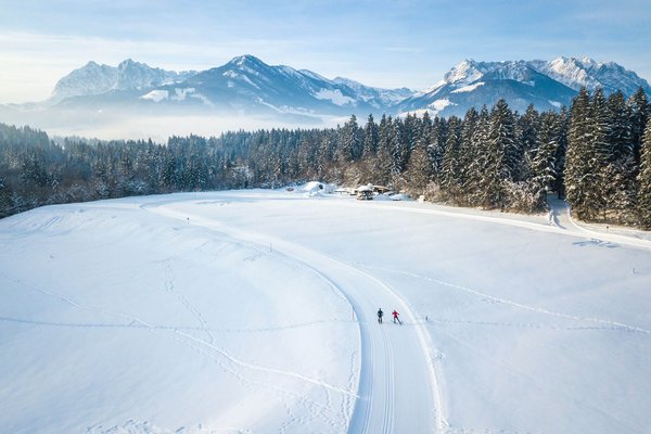Österreich © Tourismusverband Kaiserwinkl Zwei Skifahrer auf verschneiter Loipe vor verschneiten Bergen und Wald