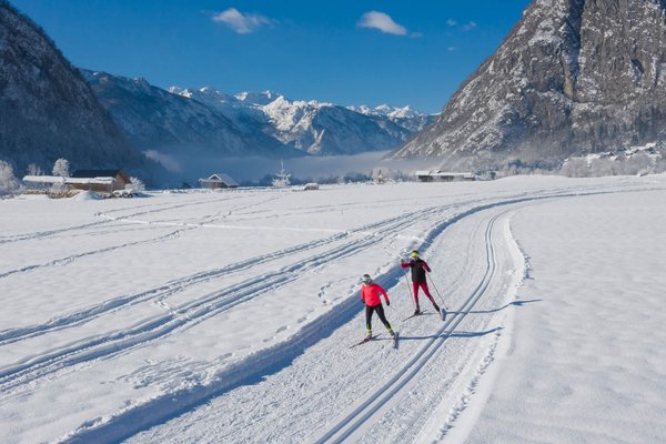 Slowenien © Mojca Odar Zwei Langläufer auf schneebedeckter Loipe vor Bergen bei blauem Himmel