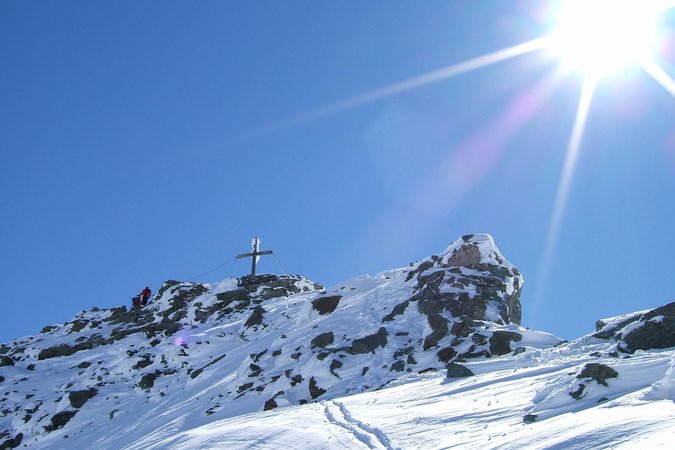 Langlauf Urlaub © Andreas Kleinwächter Schneebedeckter Berggipfel mit Gipfelkreuz und zwei Wanderern unter hellem Sonnenschein