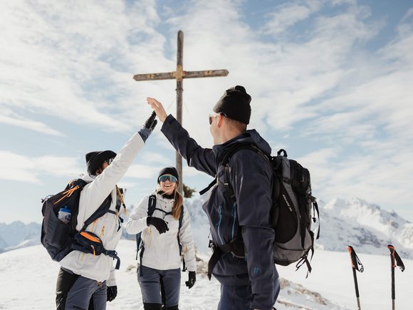 Langlauf Urlaub © Alex Moling Drei Wanderer geben sich im Schnee an einem Gipfelkreuz einen High Five