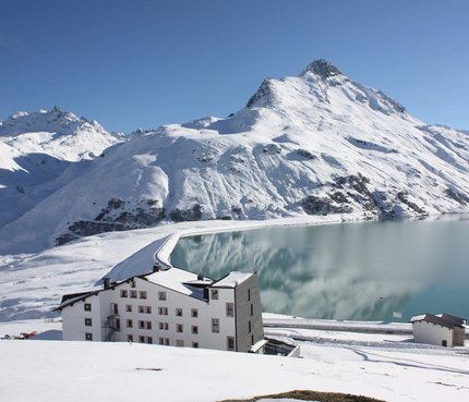 Berggasthof Piz Buin © Berggasthof Piz Buin GmbH Schneebedeckte Berge und See mit weißem Gebäude im Vordergrund