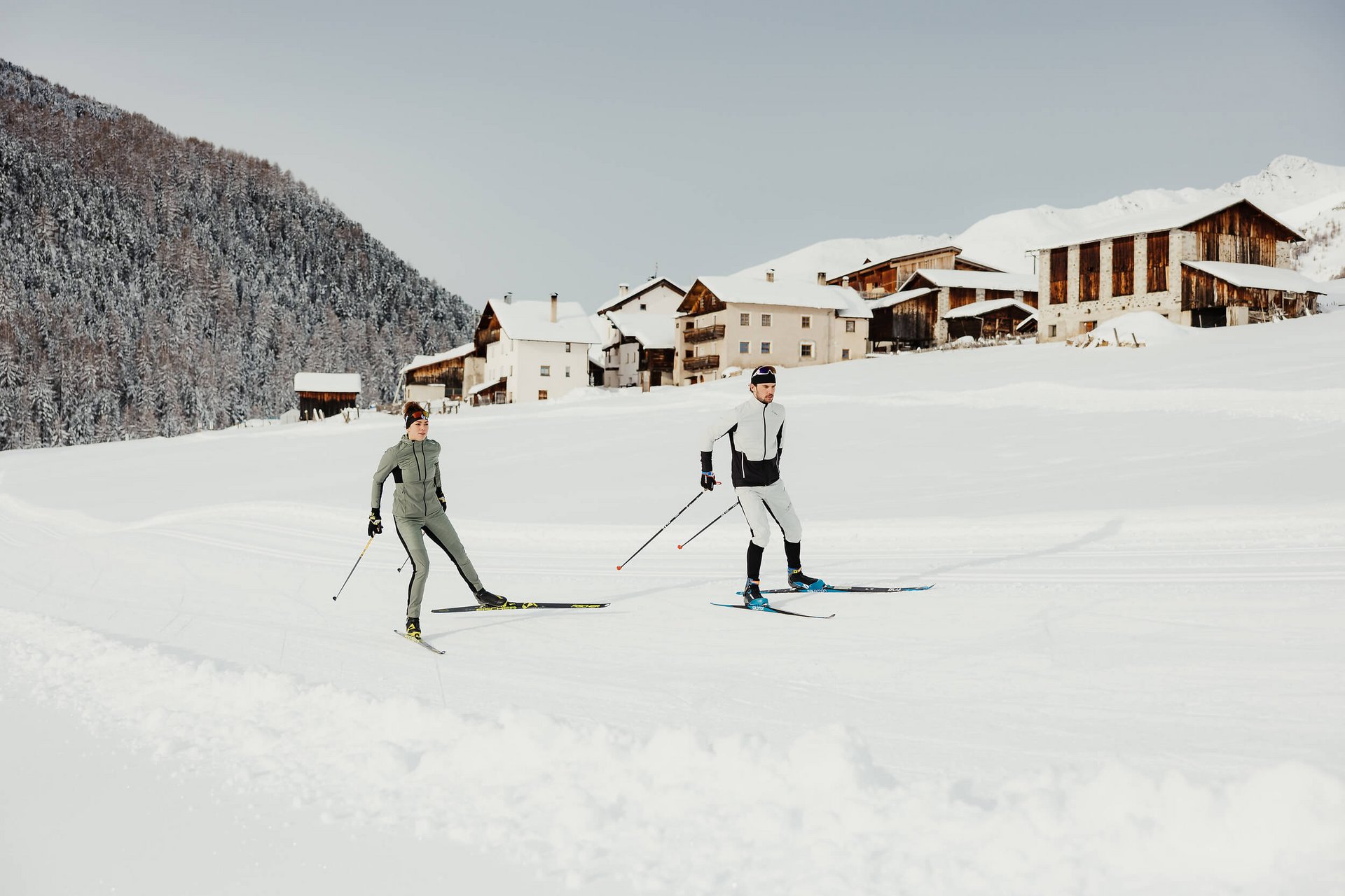 Langlauf Urlaub © Alex Moling Zwei Skifahrer beim Langlauf vor verschneiten Häusern und Wald