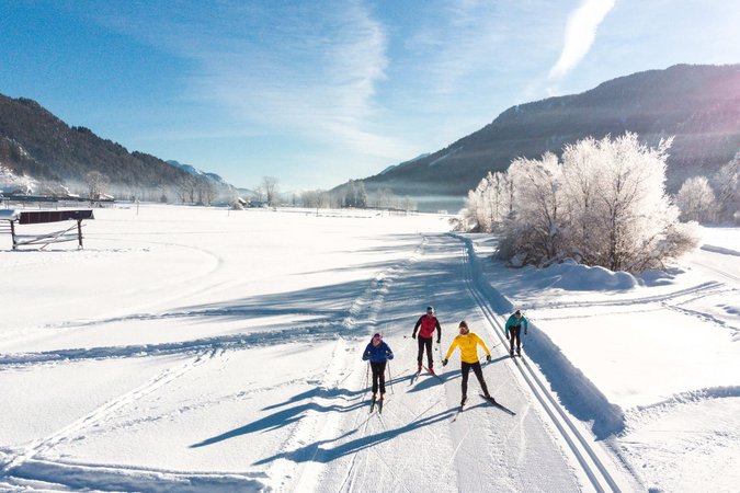 Langlauf Urlaub © Nordic Center Planica Vier Skifahrer auf einer Loipe in winterlicher Berglandschaft bei Sonnenschein