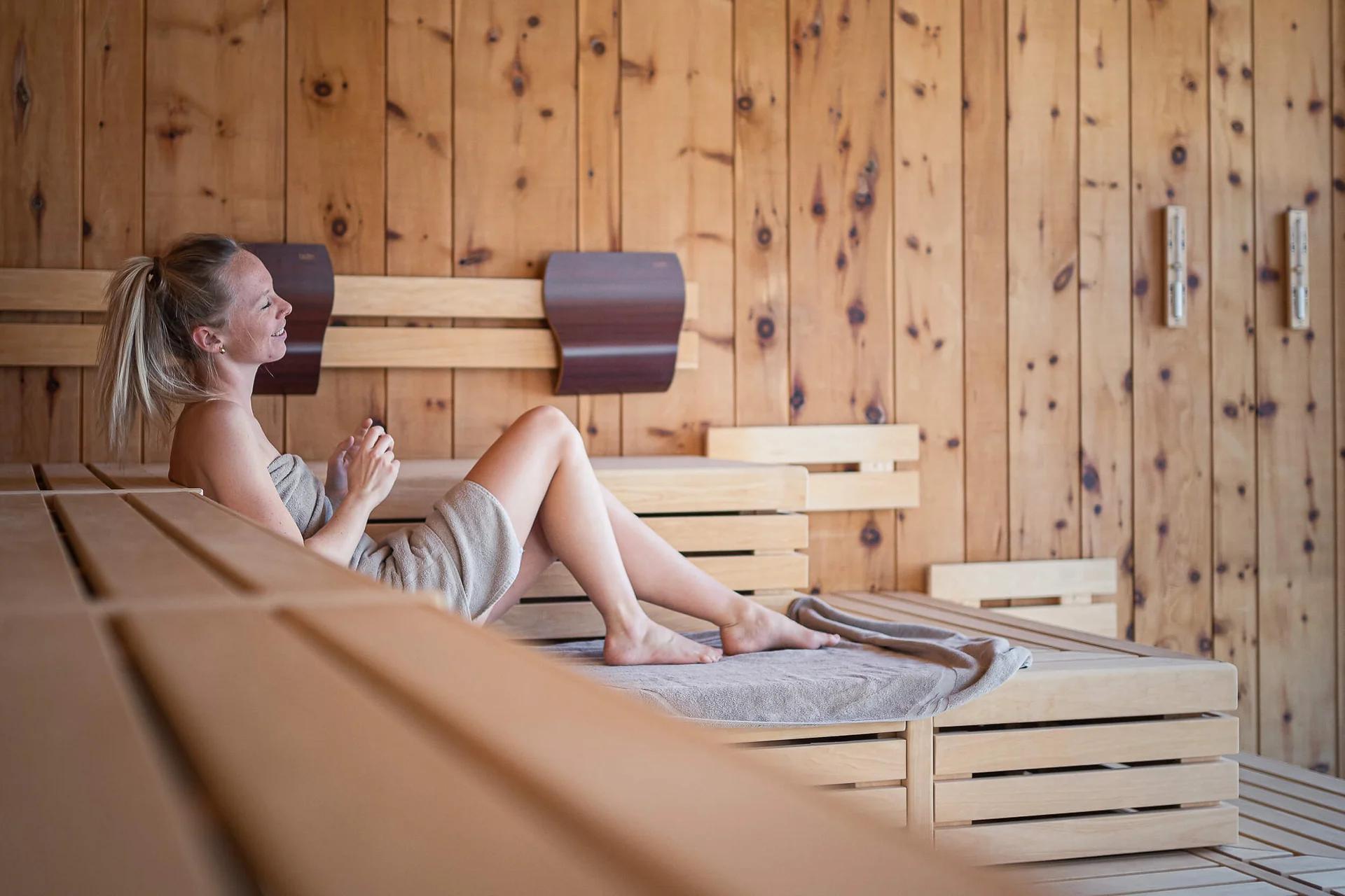 Langlauf Urlaub © socialventures Frau entspannt in Sauna auf Handtuch auf Holzbank