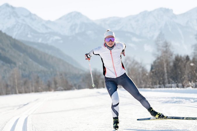 Langlauf Urlaub © Josef Plaickner Langläuferin in weißer Jacke auf verschneiter Loipe vor Bergen