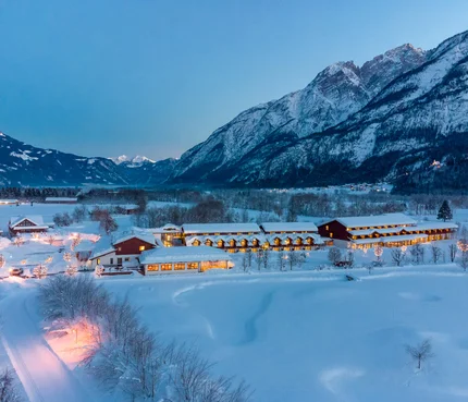 Dolomitengolf Hotel & Spa © Martin Lugger Verschneite Häuser im Tal vor beleuchteten Bergen bei Dämmerung