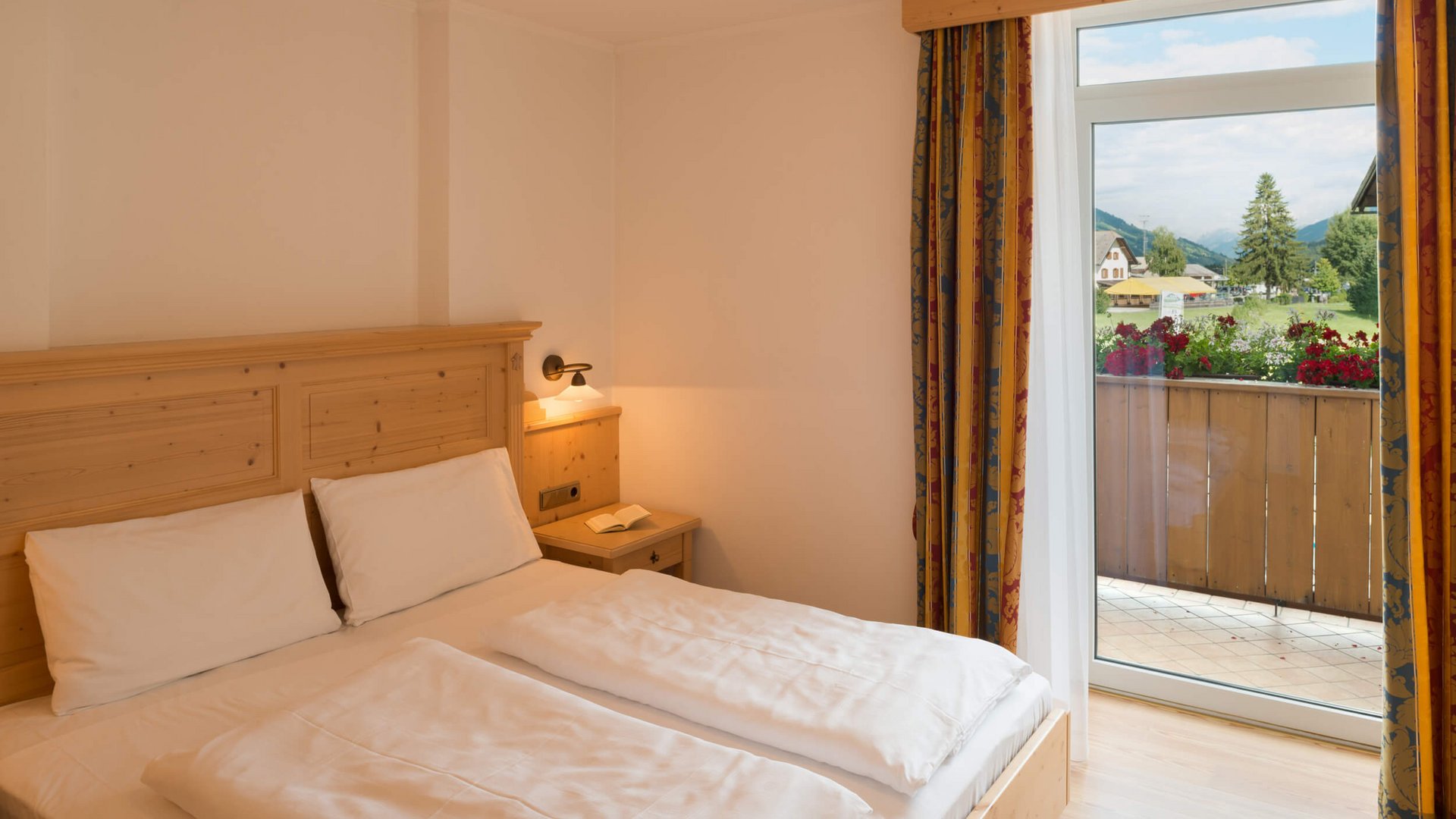 Apparthotel Germania *** © Apparthotel Germania GmbH Gemütliches Hotelzimmer mit Doppelbett und Blick auf Balkon und Landschaft