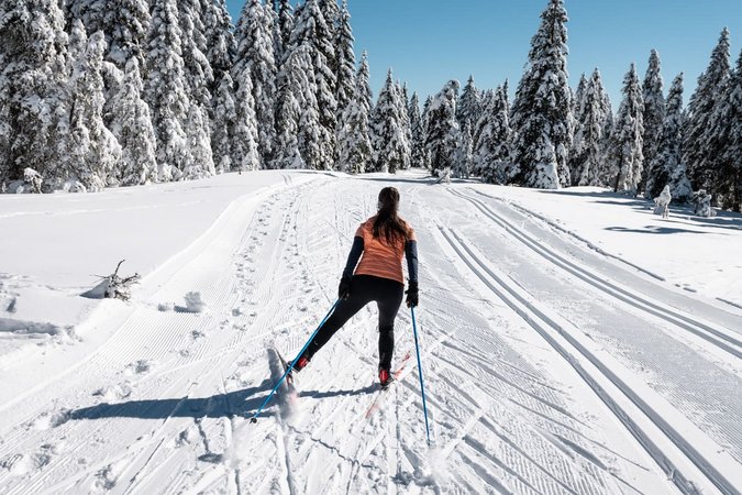 Langlauf Urlaub © Daniel Hug Frau beim Skilanglauf auf verschneiter Winterlandschaft mit Tannenbäumen