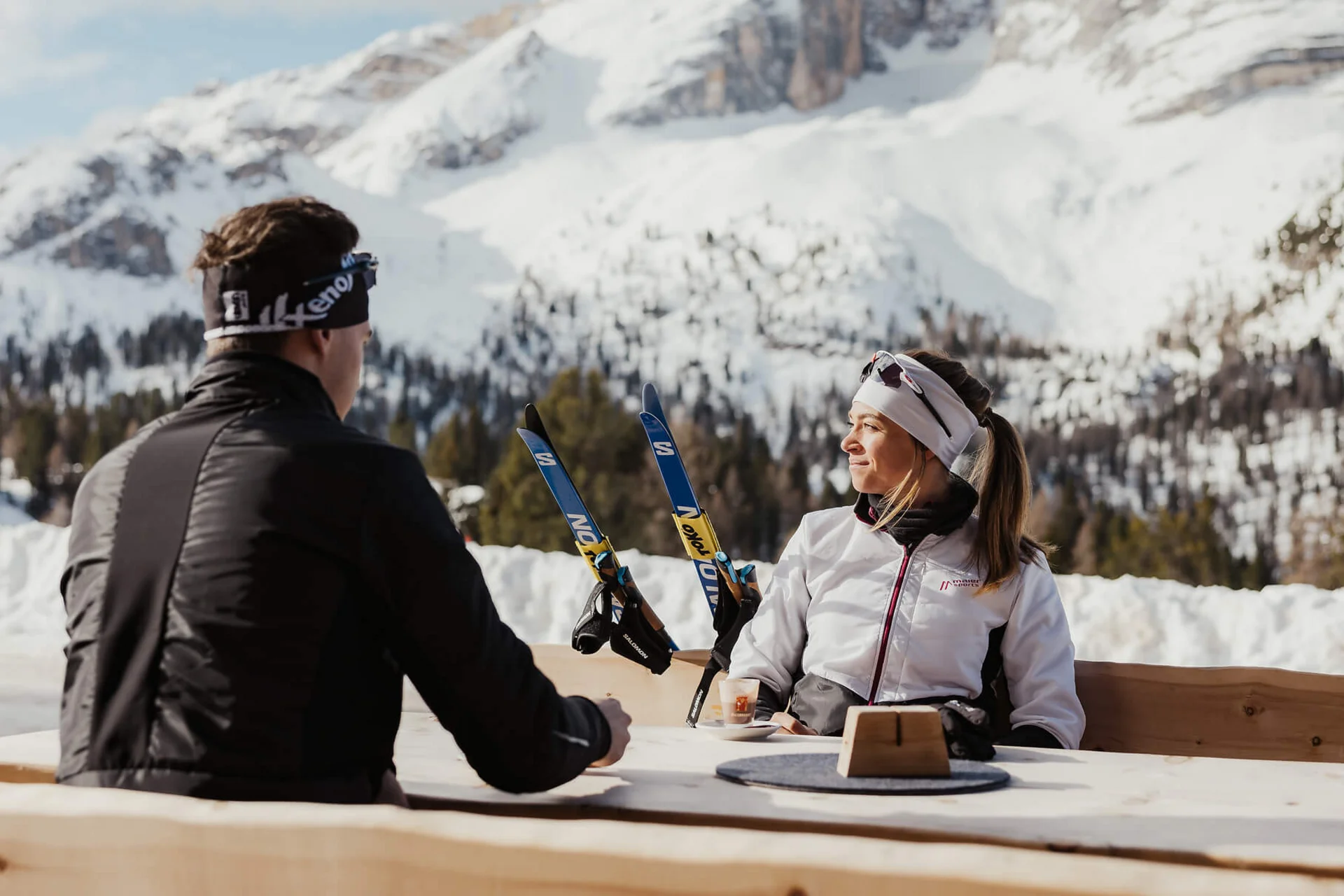 Langlauf Urlaub © Alex Moling Zwei Personen sitzen draußen mit Skiern vor schneebedeckten Bergen