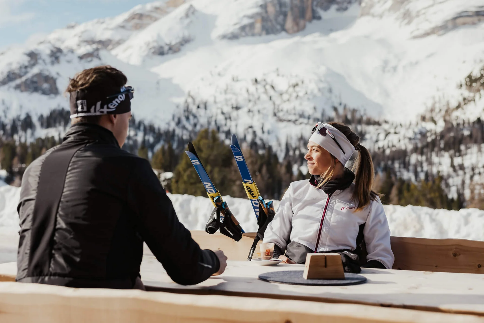 Langlauf Urlaub © Alex Moling Zwei Personen sitzen draußen mit Skiern vor schneebedeckten Bergen