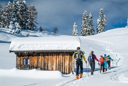 Sarntal – Skitouren im Herzen Südtirols © Carmen Moser Gruppe Skitourengeher wandert im Schnee an einer verschneiten Holzhütte vorbei