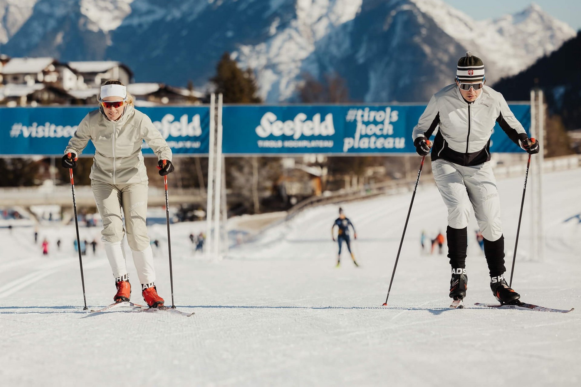Langlauf Urlaub © Alex Moling Zwei Langläufer auf der Loipe mit schneebedeckten Bergen im Hintergrund