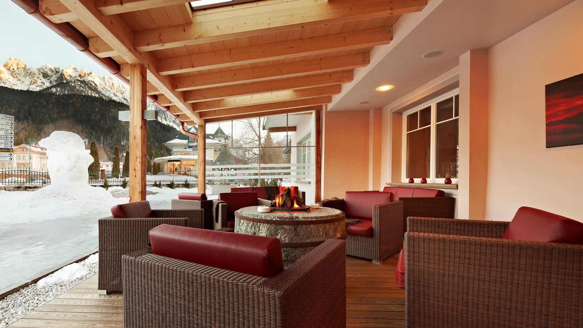 Apparthotel Germania *** © Apparthotel Germania GmbH Überdachte Sitzgruppe mit Kamin vor schneebedeckten Bergen und Schneedekoration