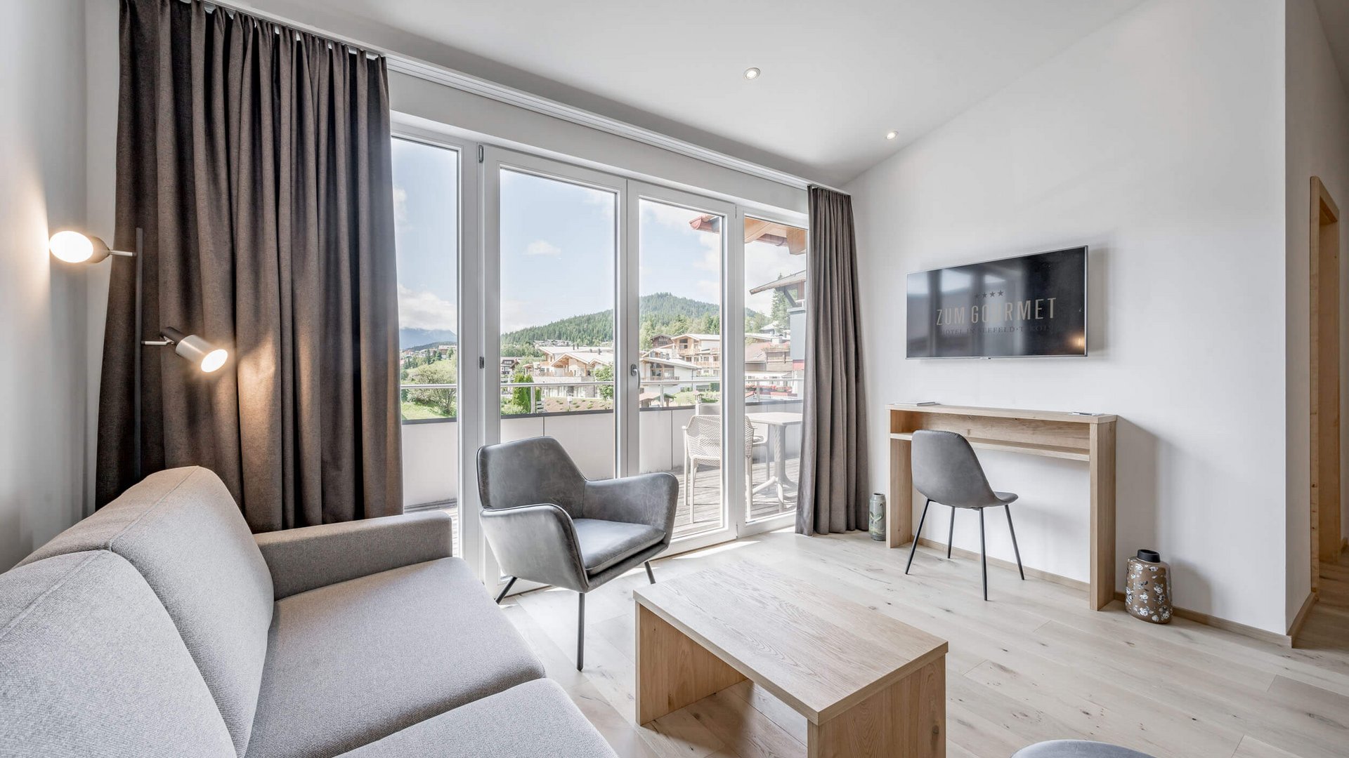 All Inclusive Hotel zum Gourmet **** © Stephanie Lohmann Modernes Wohnzimmer mit grauem Sofa, Sessel, TV und Balkon mit Bergblick