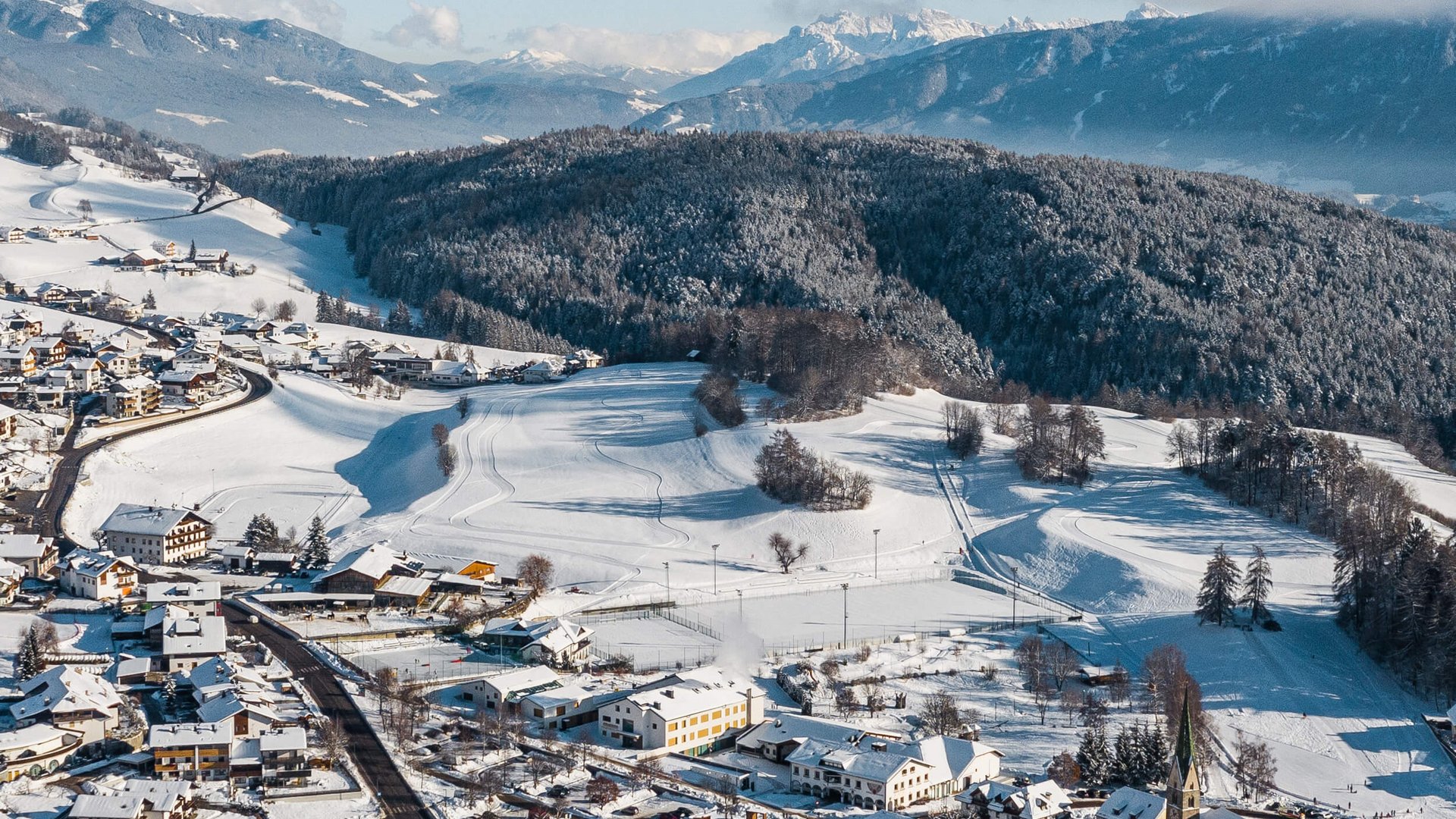 Langlauf Urlaub in Gitschberg-Jochtal © Hannes Niederkofler Verschneites Dorf zwischen bewaldeten Hügeln und Bergen im Hintergrund