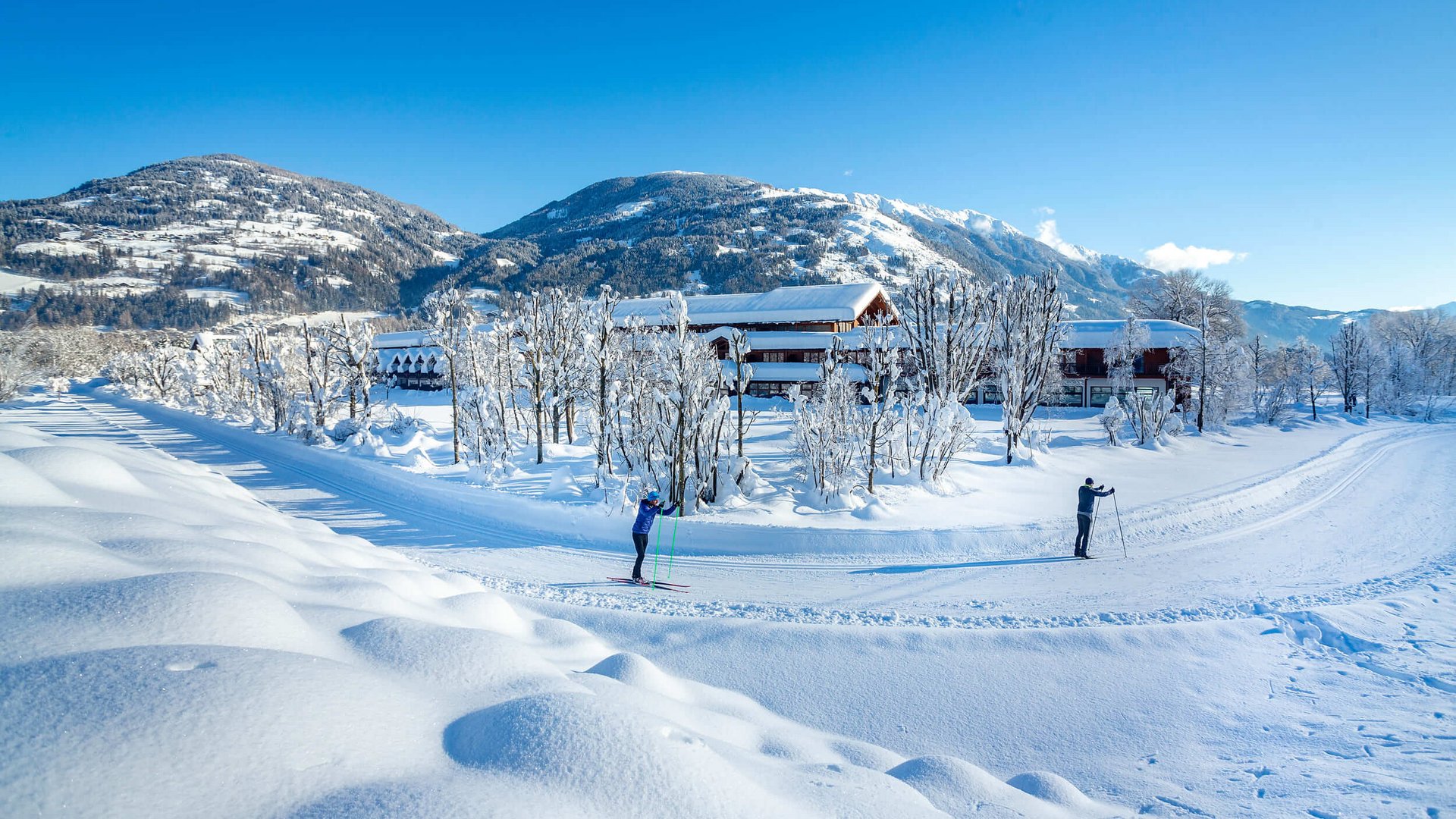Langlauf Urlaub in Osttirol © Martin Lugger Zwei Skifahrer auf verschneiter Loipen vor Berglandschaft und Häusern
