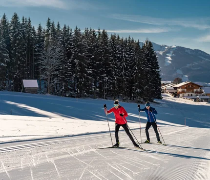 Fis Weltcup Nordische Kombination © TVB Schladming Dachstein - Christine Höflehner Zwei Langläufer auf verschneiter Loipe vor Wald und Bergen