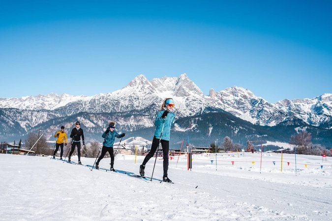 Langlauf Urlaub © Michael Geißler Gruppe beim Langlaufen vor schneebedeckten Bergen unter blauem Himmel