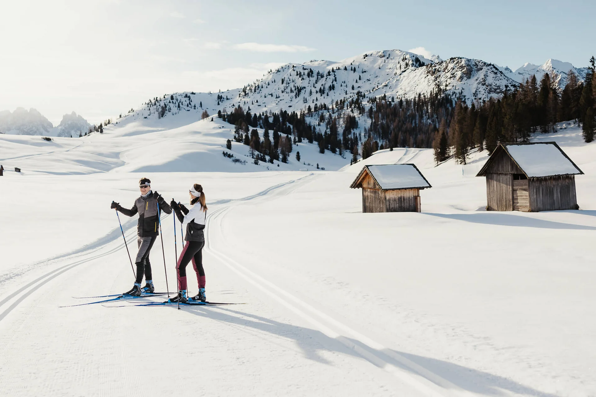 Langlauf Urlaub © Alex Moling Zwei Langläufer auf verschneiter Loipe mit Hütten und Bergen im Hintergrund