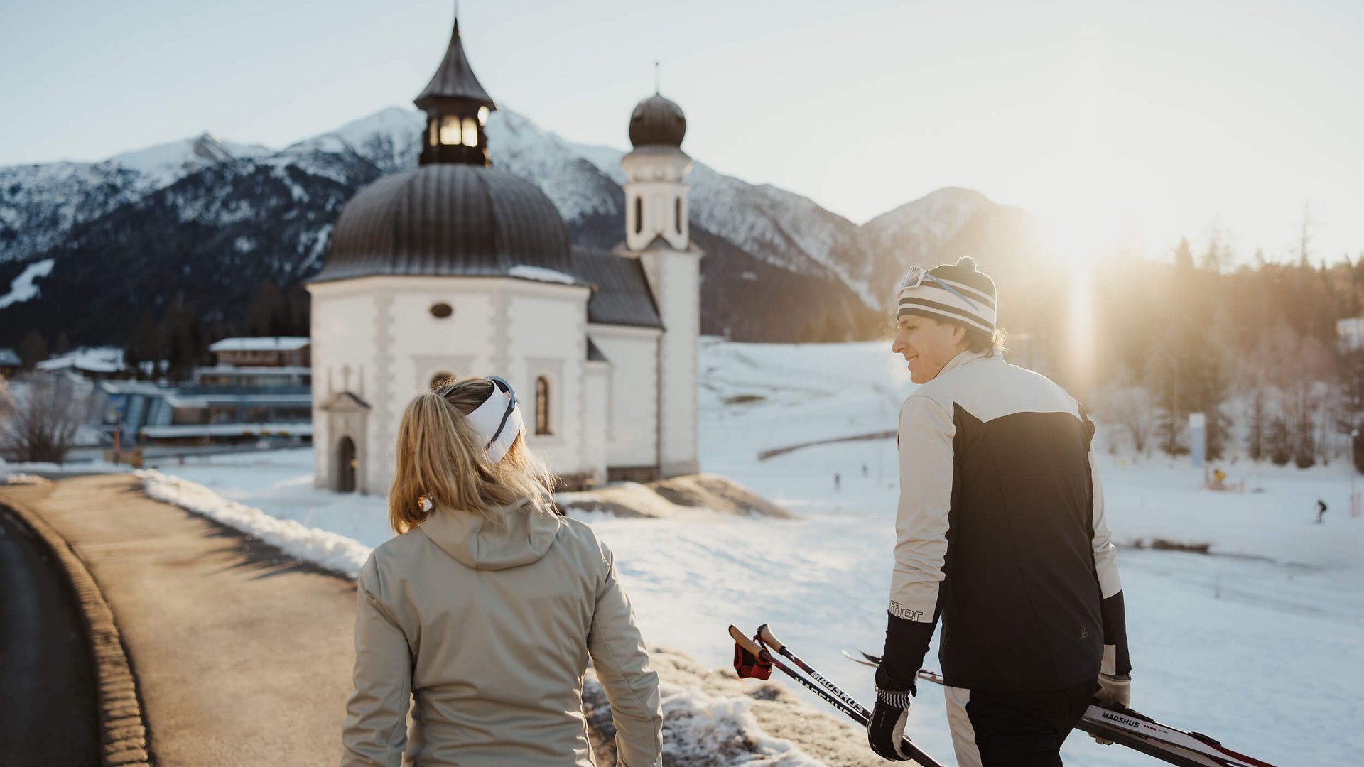 Langlauf Urlaub © Alex Moling Zwei Langläufer im Winter vor einer Kirche in den Bergen bei Sonnenuntergang