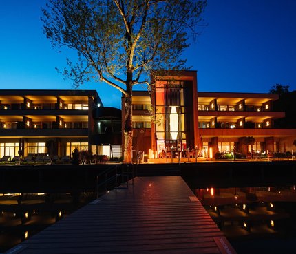 Das Walchsee Resort © Pletzer Resorts Beleuchtetes modernes Hotel bei Nacht mit Wasserspiegelung und Steg