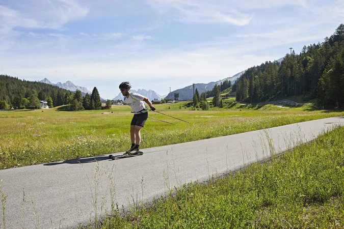 Langlauf Urlaub Mann beim Rollerski in einer grünen Berglandschaft auf einem Asphaltweg