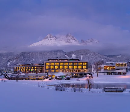 Ritzenhof - Hotel und Spa am See © Stefan Gimpl Beleuchtetes Hotel im verschneiten Tal vor bewölktem Berggipfel bei Abenddämmerung