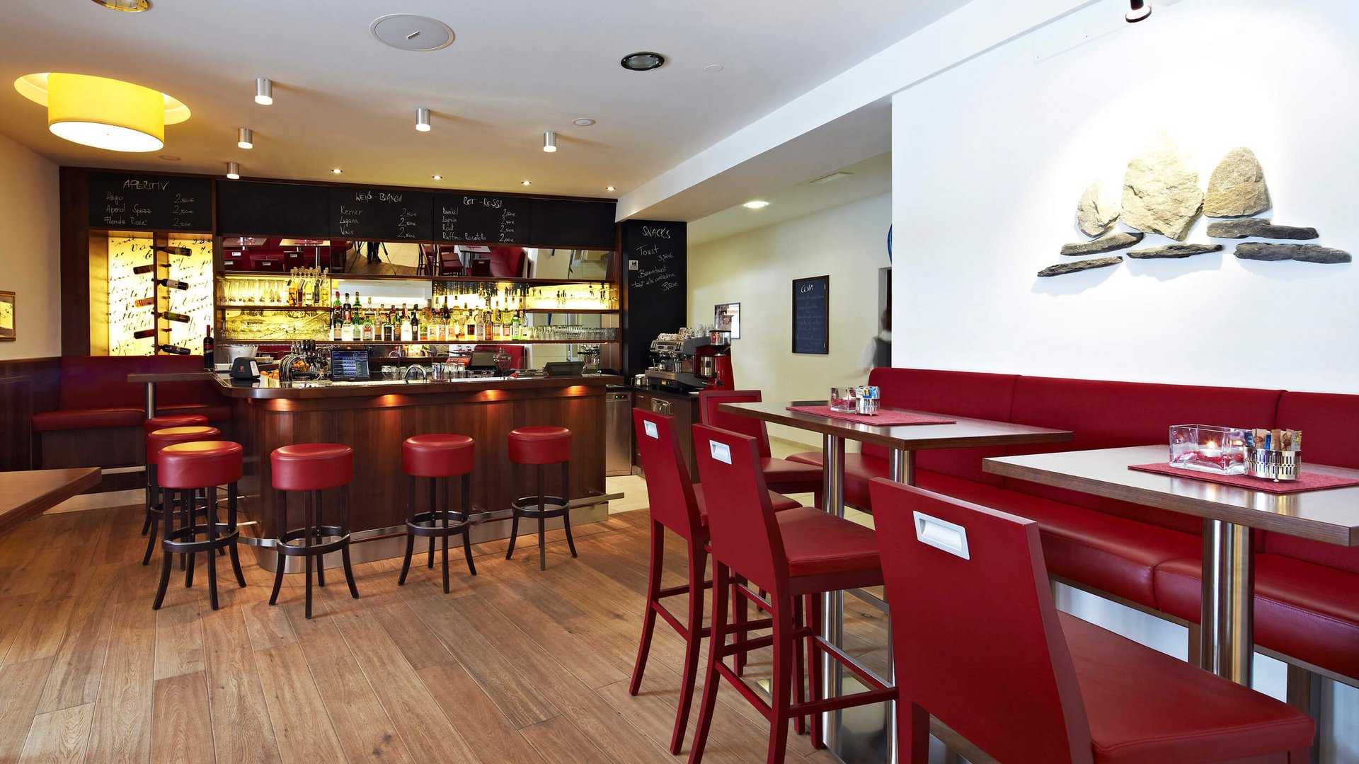 Apparthotel Germania *** © Apparthotel Germania GmbH Moderner Barbereich mit roten Sitzgelegenheiten und Holzfußboden