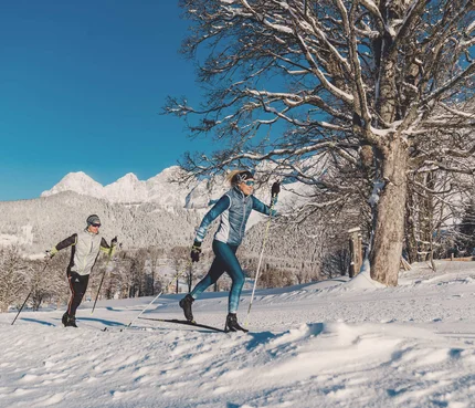 Dachsteinlauf 2026 © TVB Schladming Dachstein - Christine Höflehner Zwei Personen beim Langlaufen vor verschneiten Bergen und klarem Himmel