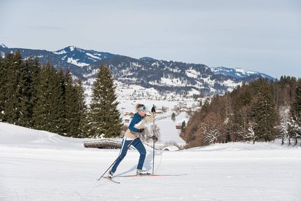 Winterwunderland Oberstdorf © Frithjof Kjer Frau beim Langlauf im verschneiten Gebirge mit Tannenbäumen im Hintergrund