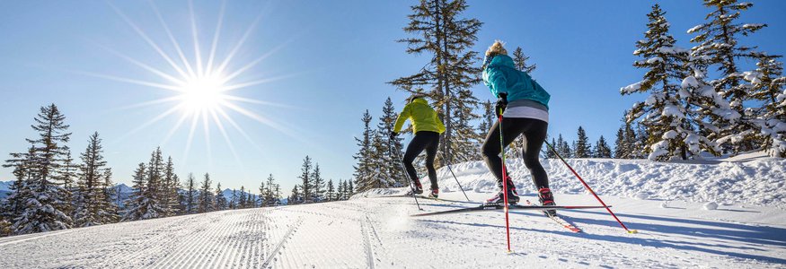 Filzmoos © Christian Fischbacher - Filzmoos Tourismus Zwei Skilangläufer im Sonnenschein auf schneebedeckter Strecke mit Bäumen