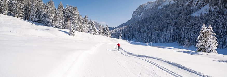 Winterurlaub in Bayern © Tourismus Oberstdorf - Eren Karaman Langläufer in roter Jacke auf schneebedeckter Loipe in verschneiter Winterlandschaft
