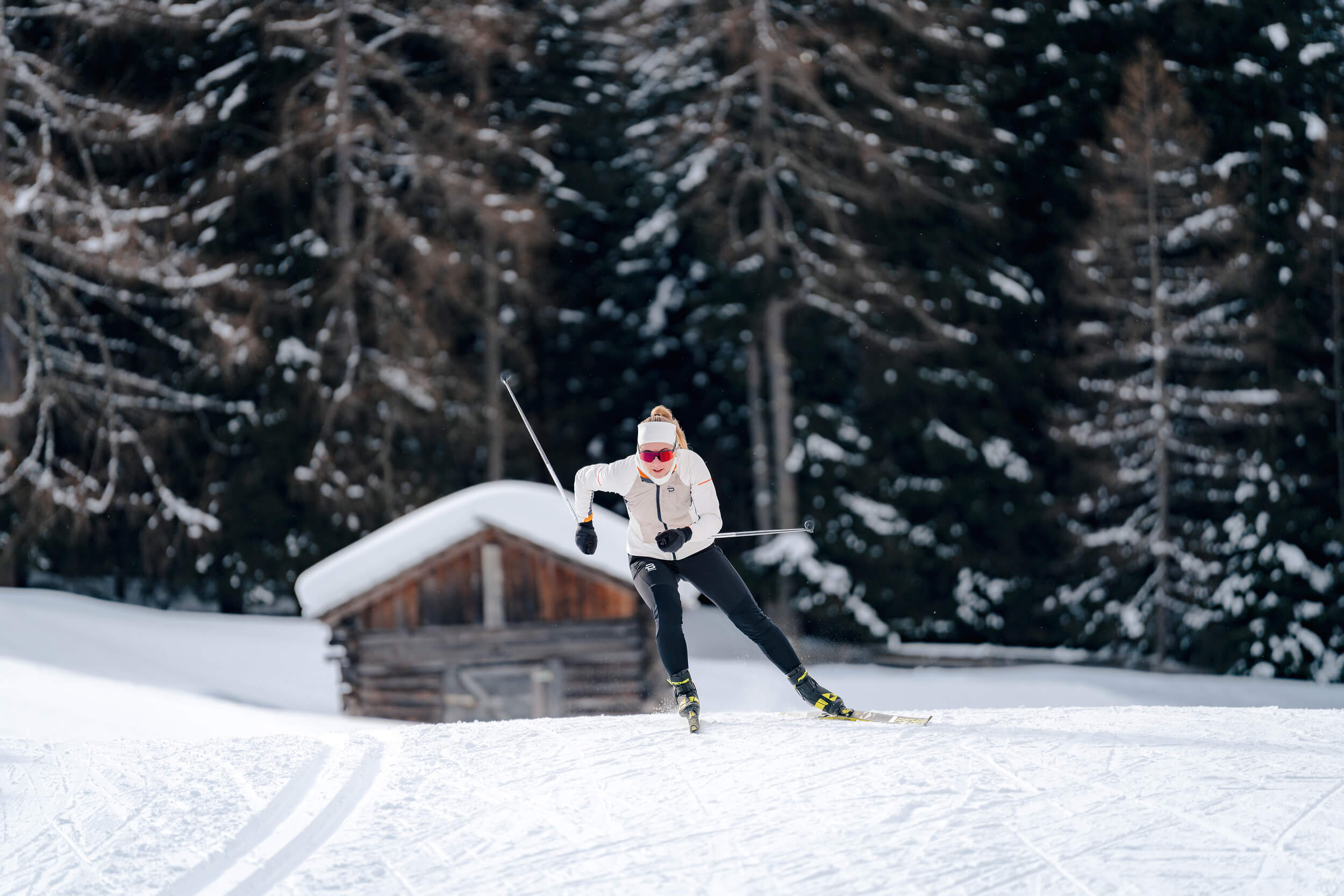 Dolomitenregion Kronplatz © Josef Plaickner Frau beim Langlaufen vor verschneiter Hütte und Wald